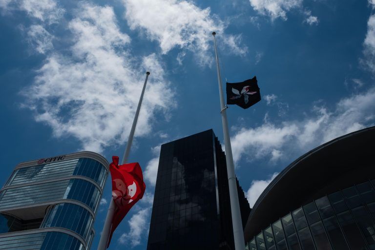 Iza de la bandera negra/blanca del movimiento de protesta en Hong Kong mientras retiran la bandera roja/blanca oficial de la ciudad